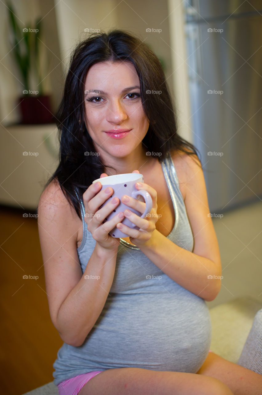 Portrait of pregnant woman holding cup of coffee at home
