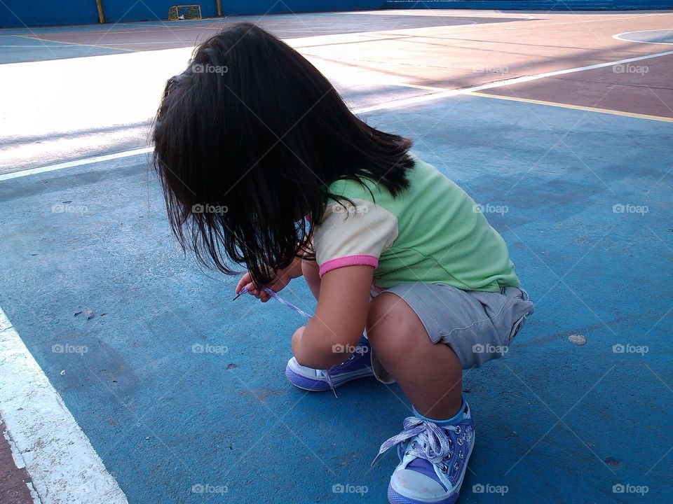 Inocencia, bebe intentando amarrar su zapato sin tener idea de como hacerlo. Después de hacer deporte esta niña hace el intento de amarrar su calzado.