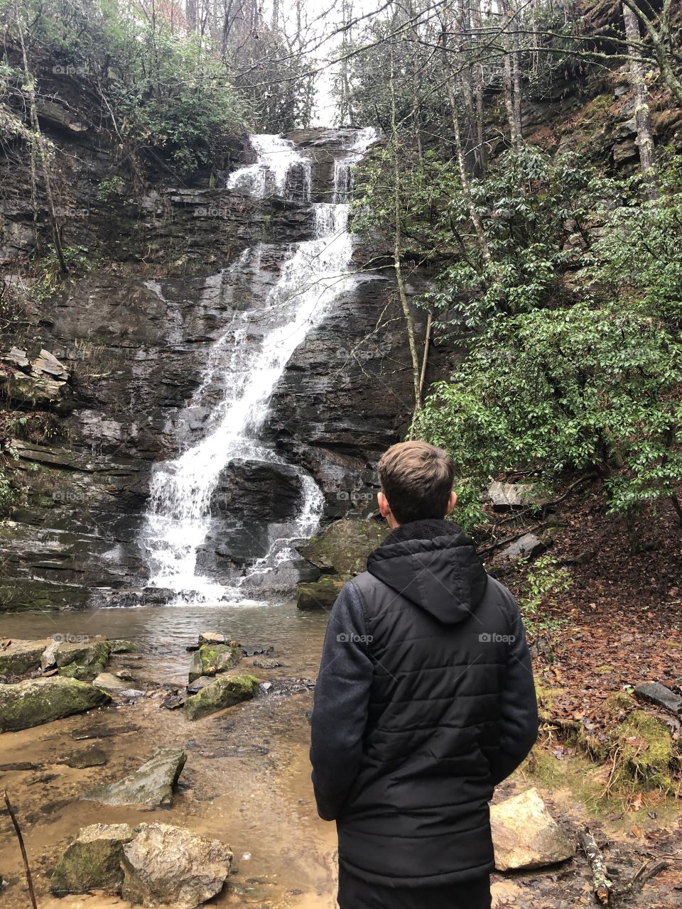 Teenage boy standing in front of large waterfall 