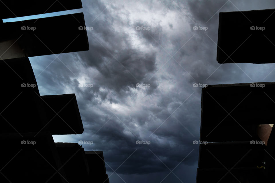 A low angle perspective seen from ground level through stacked picnic tables reveals an ominous sky with threatening storm clouds.