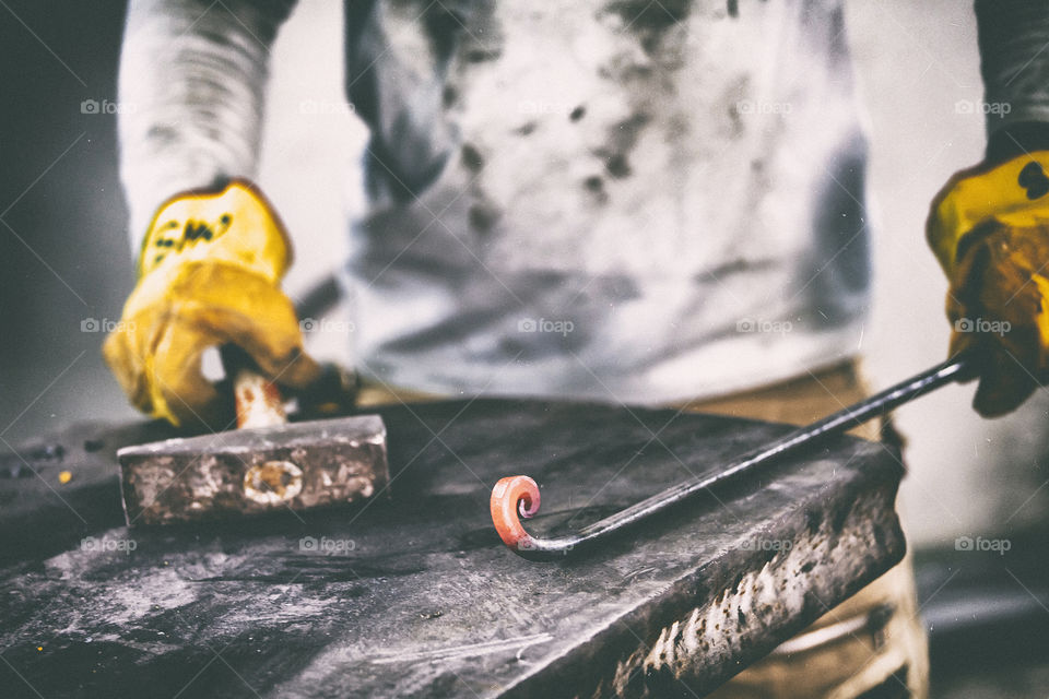 Closeup of blacksmith hand holding tongs with metal piece heated in fire before forging, selective focus. Blacksmithing concept.