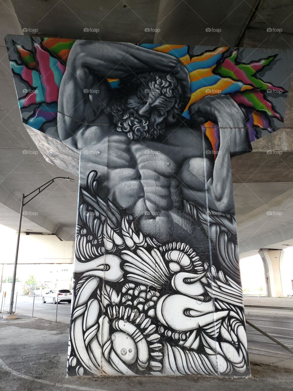 Visual street art on cement highway pillar under highway in a parking lot. Appears to be greek God of mythology Zeus.