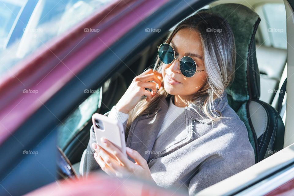 Young stylish woman with long blonde hair and sunglasses driving car