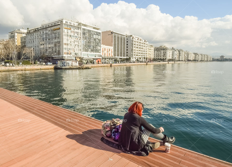 Young Woman With Her Baggage Sitting Alone At The Dock Drinking Coffee And Enjoying The View
