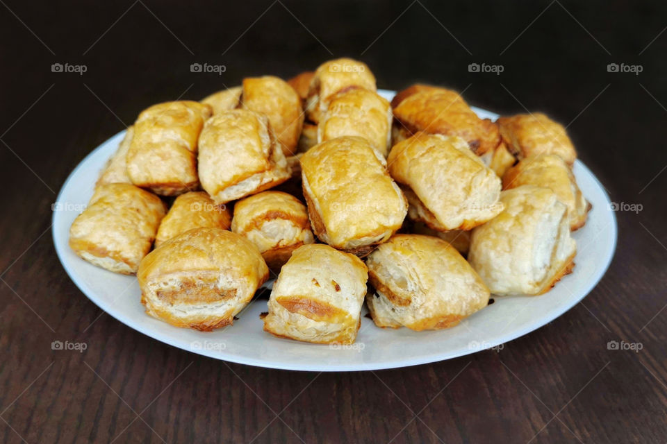Sausage rolls in a white plate on wood table.