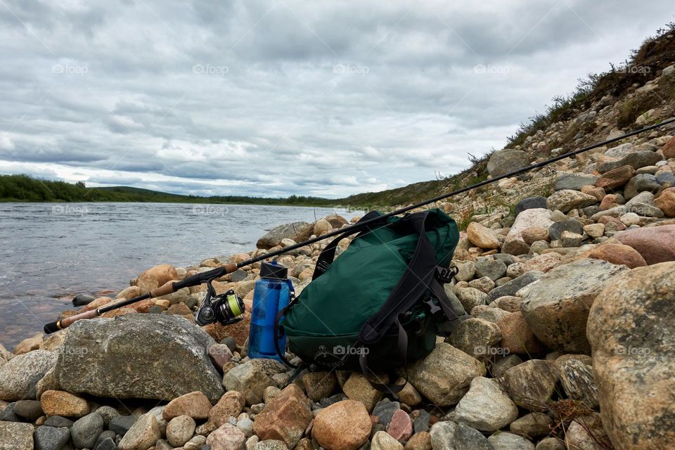Backback, water bottle with filter and fishing tackle by Lainio river in Swedish Lapland on overcast summer day.