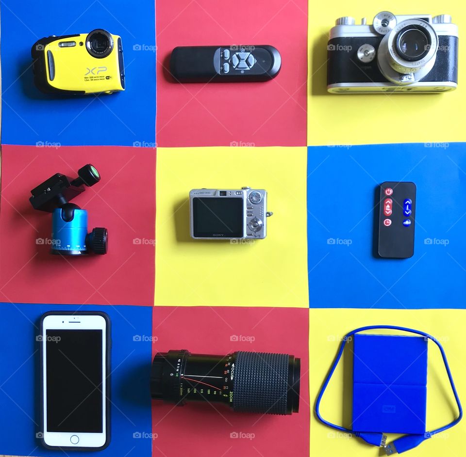 Flat lay with several types of cameras and equipment on a colorful squares