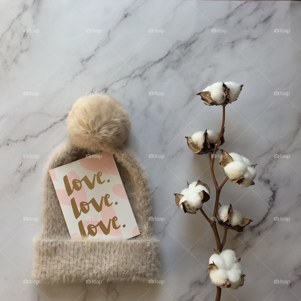 Flat lay items. Winter hat, card with inscription love, cotton flower lying on marble background 