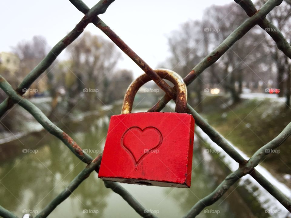 Red padlock with a heart on it hanging on the bridge in winter