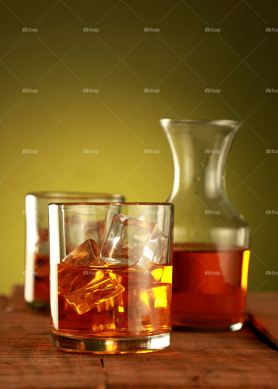 Chilled glass of whisky / whiskey with ice cubes on yellow background