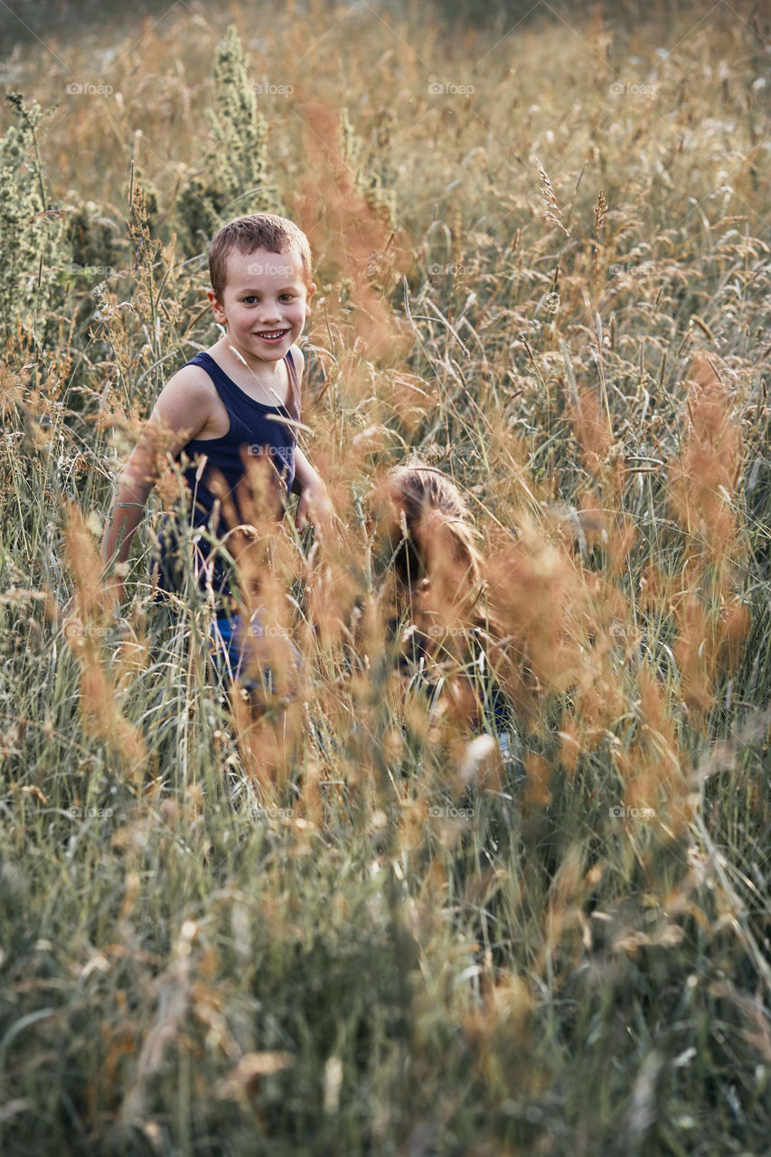 Little happy smiling kids playing in a tall grass in the countryside. Candid people, real moments, authentic situations