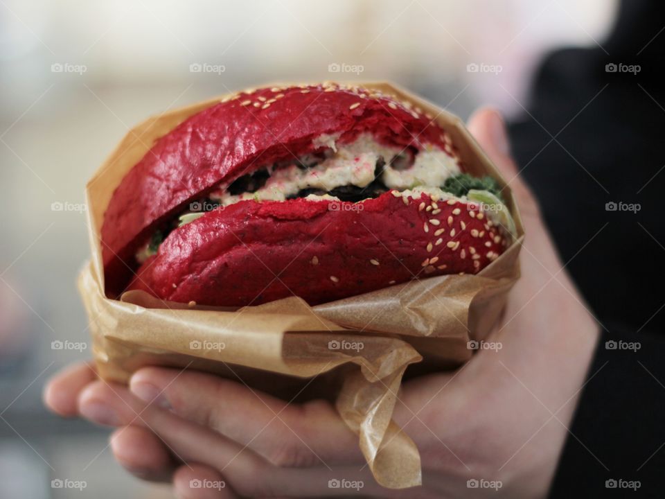 Close-up of male hands holding a red vegan burger wrapped in paper