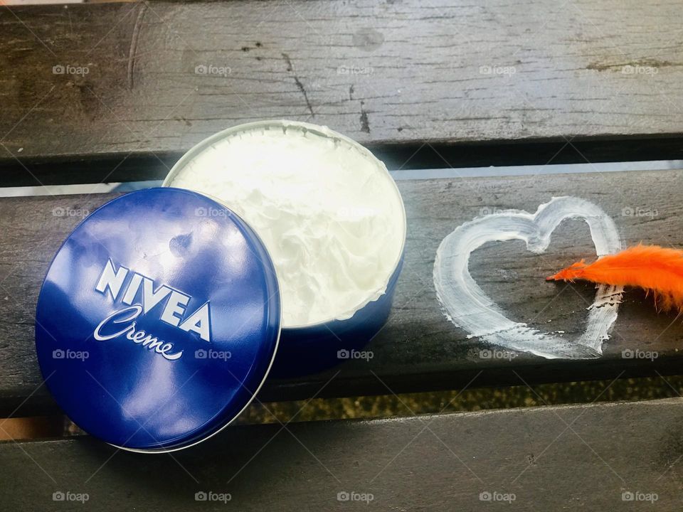 The cap of Nivea cream is open beside that a love symbol drawing with Nivea cream and orange colour feather.