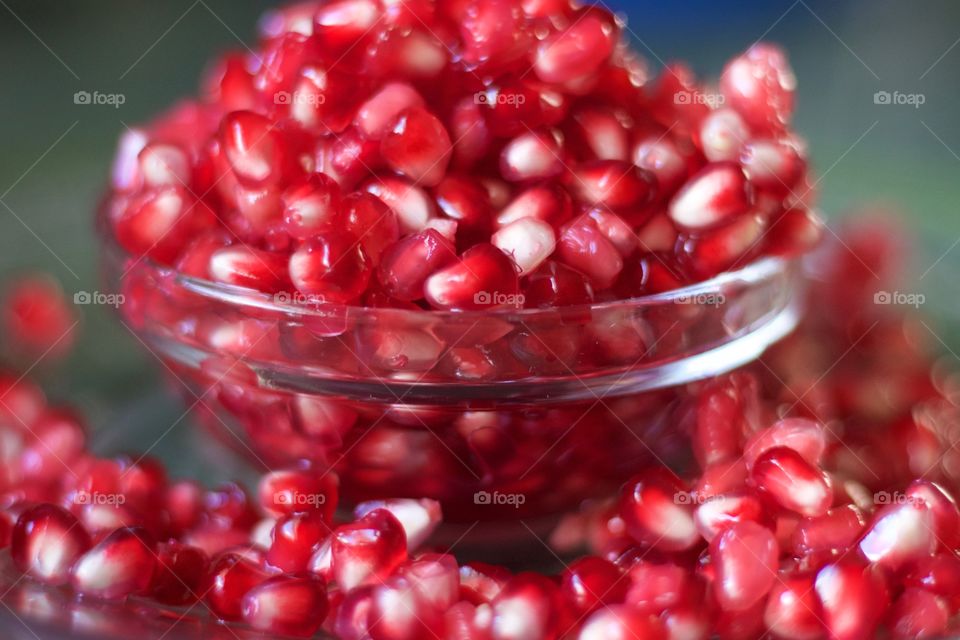 Closeup of fresh pomegranate seeds overflowing a small glass bowl against a dark background 