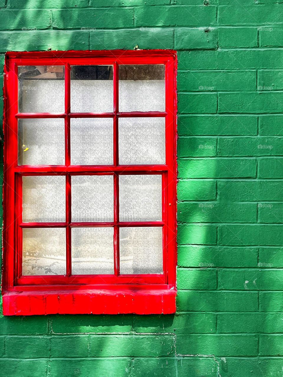 Red multi pane wood framed window on a green brick building 