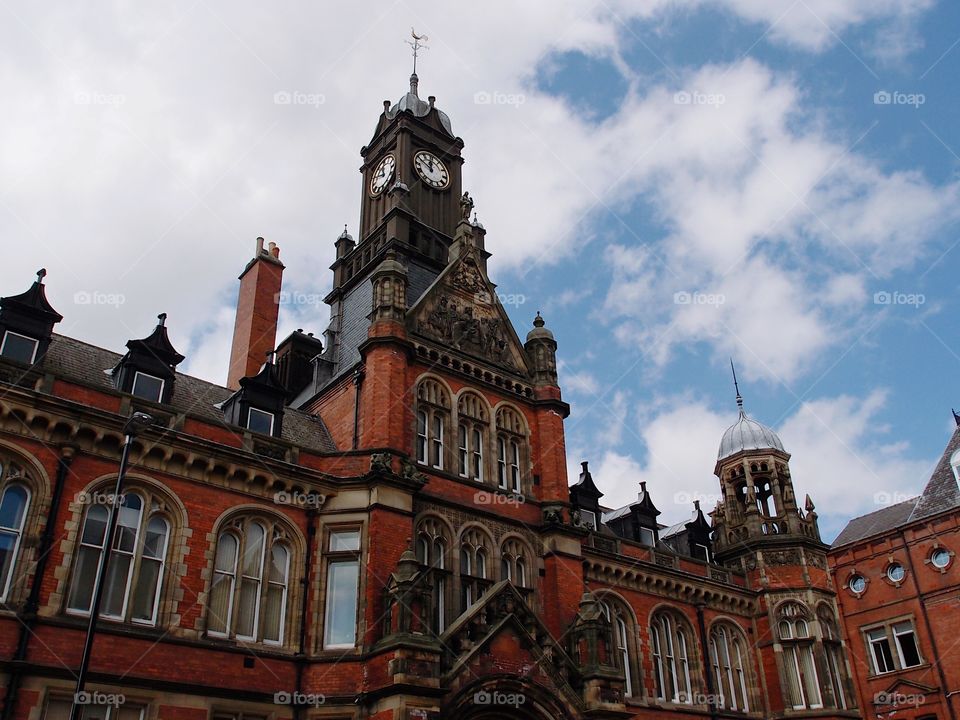 A beautiful intricately designed old brick building with lots of windows and a clock tower on a nice summer day in England. 