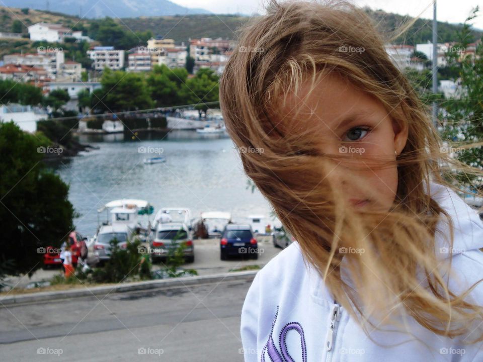 Little girl standing in the windy street. Behind is sea shore.