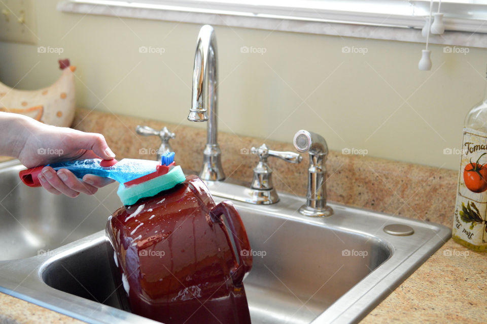 Person's hand scrubbing a pot in a kitchen sink