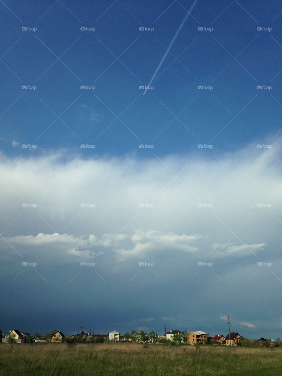 Plane line in the sky above the village in the field 