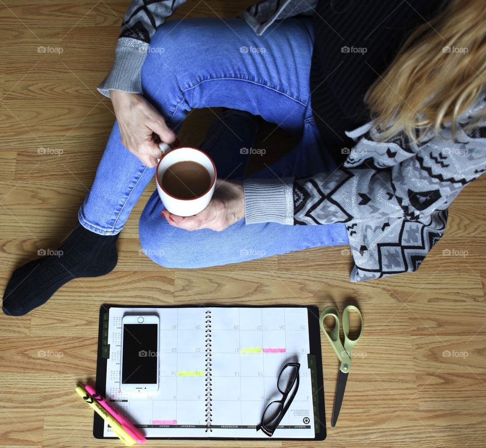 Lady sitting on the floor with a cup of coffee going over appointment calendar