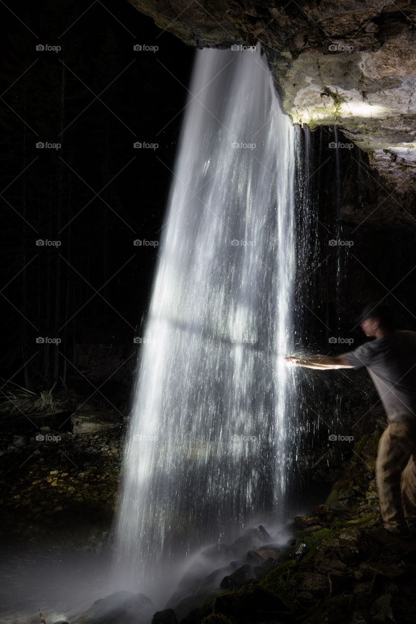 Standing behind a waterfall at night while reaching out and touching the waterfall 