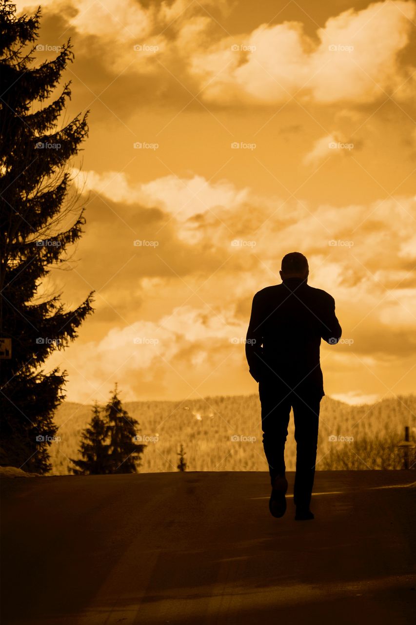 Silhouette of man walking uphill on a path through the forest