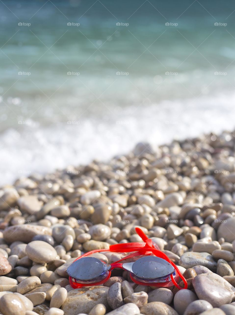 Red swimming glasses lays on the pebble beach 