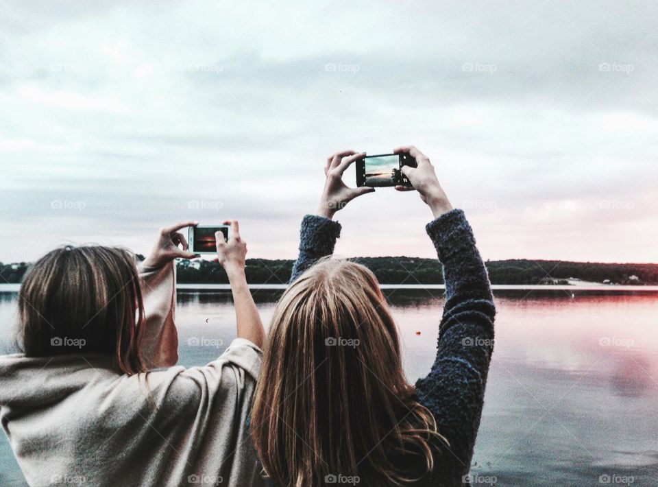 Girls friends taking pictures of the lake during sunset 