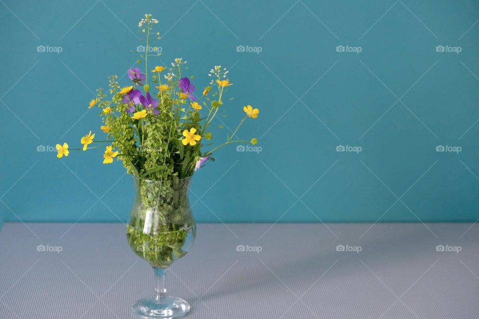 Bouquet of yellow buttercups and wildflowers in a glass on a blue background