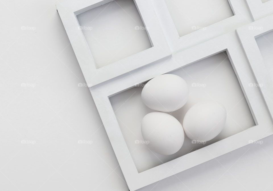 Three white eggs in a white frame on a white background, flat lay close-up. Concept white on white,monochrome, minimalism creative.