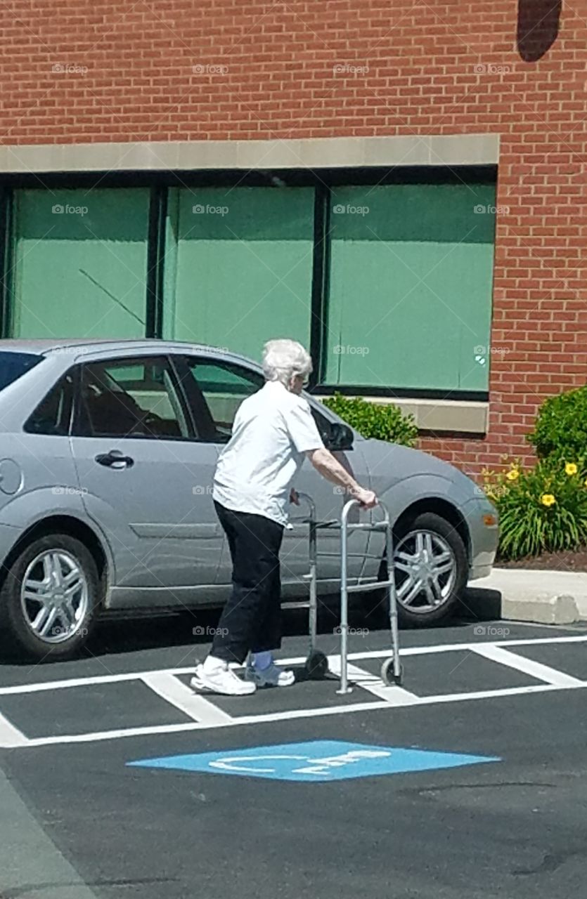 Senior citizen, older person using walker in handicap spot.