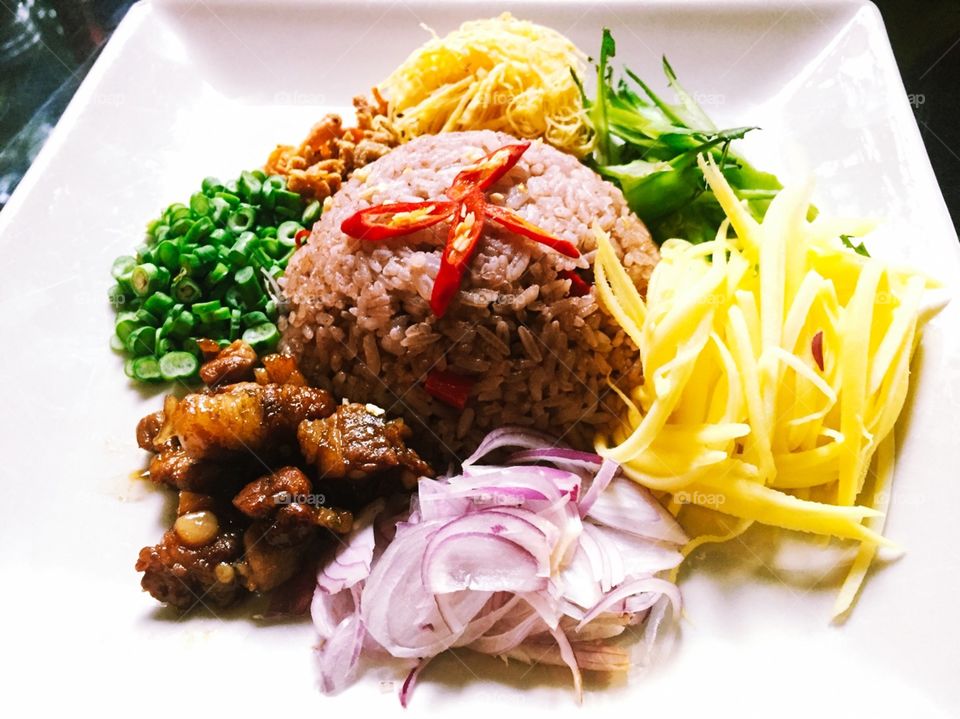 colorful dish, with brown rice, mango, dragon bean, purple onion, cowpea, fried egg, dried shrimp, bacon and garnished red  chilli 