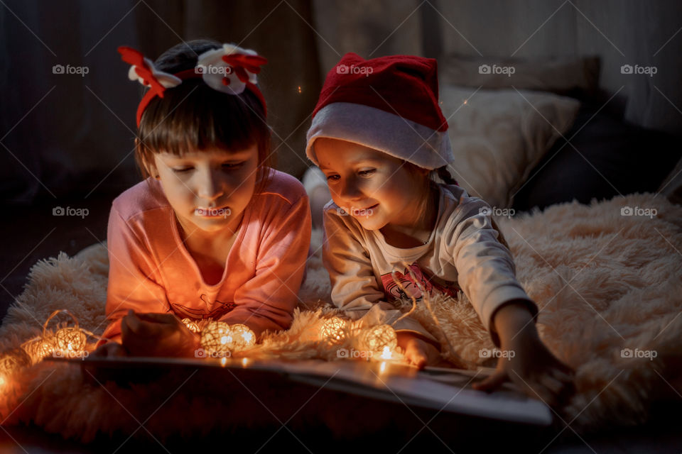 Little sisters reading a book at Christmas time 