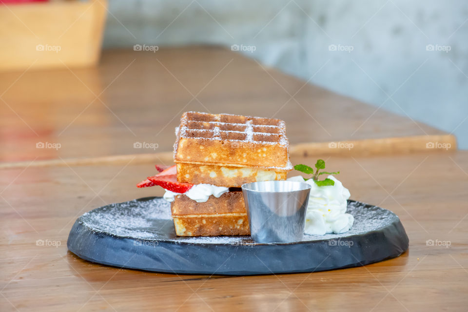 Waffle Strawerry fresh cream in the black plate on wooden table.