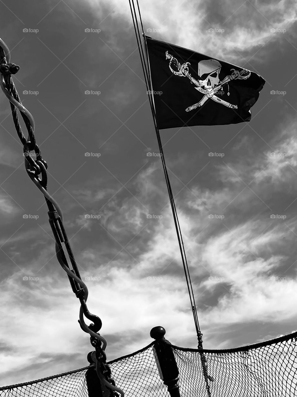 Black and white photo of the skull and cross bones flag on a pirate ship with storm clouds forming over the sea.