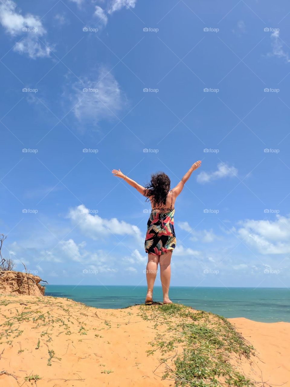 A person on top of the dunes with open arms receiving the sun and wind 