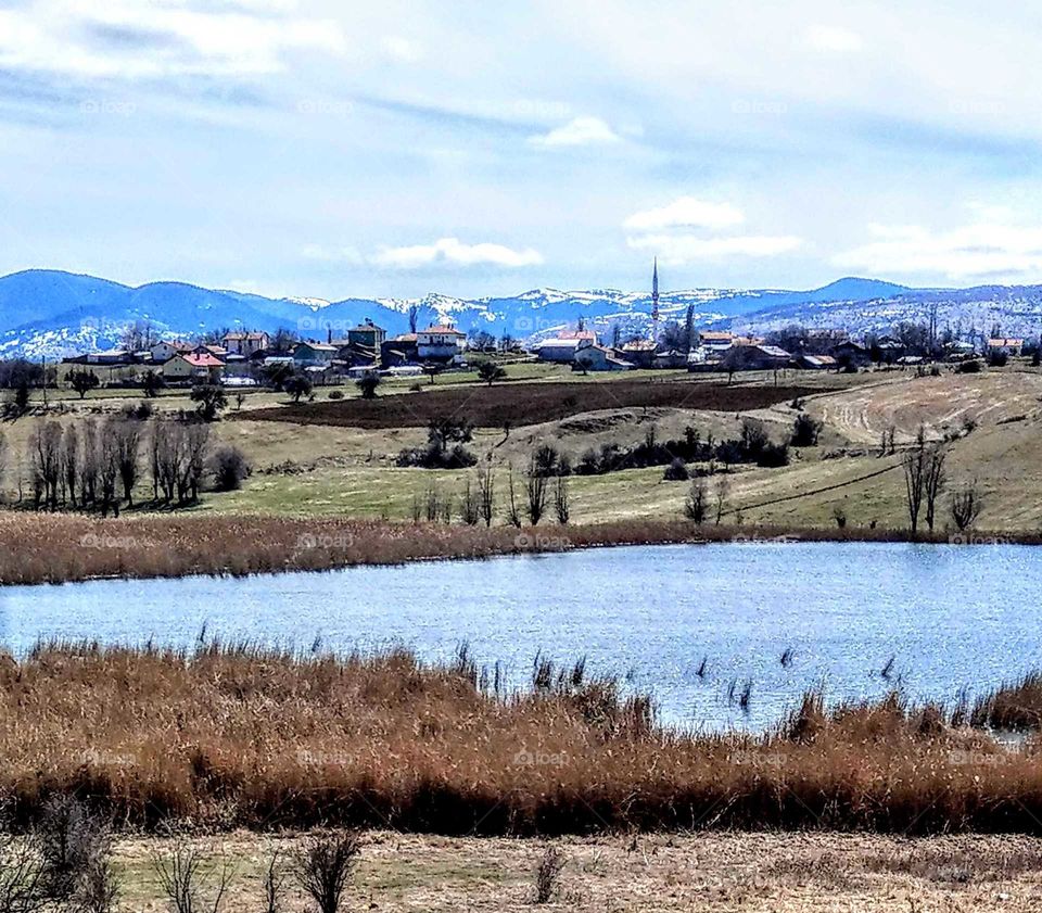 The mountain in the distance, trees, hill, lake, grass, all over are beautiful outside landscape.