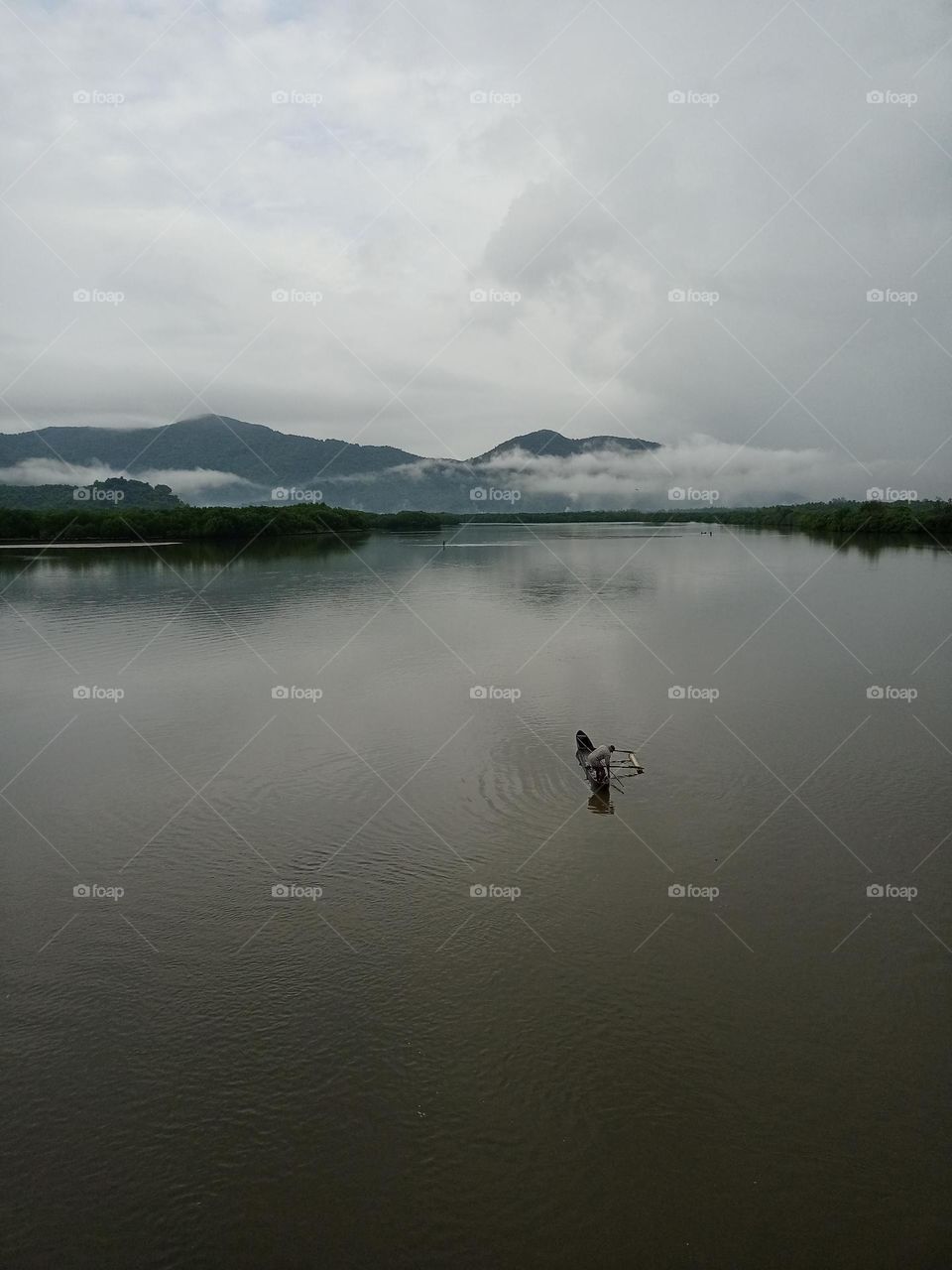 A fisherman caching the fish early in the morning in river with nice background of clouds mountain water it's lucking beautiful nature photography