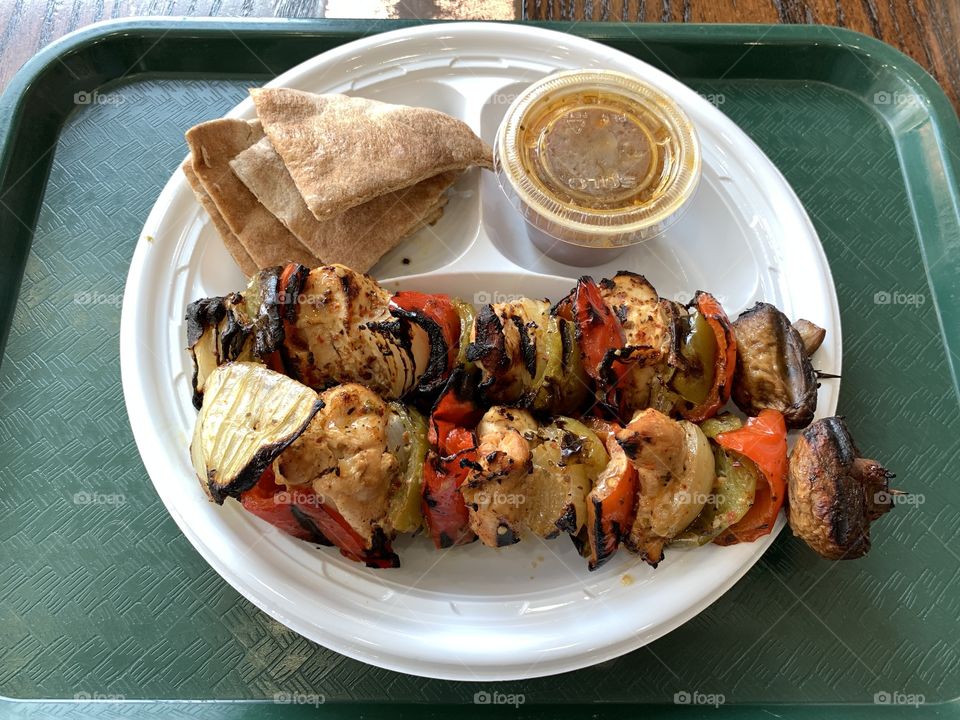 Chicken kebab with vegetables in a white round plastic plate on the green background.