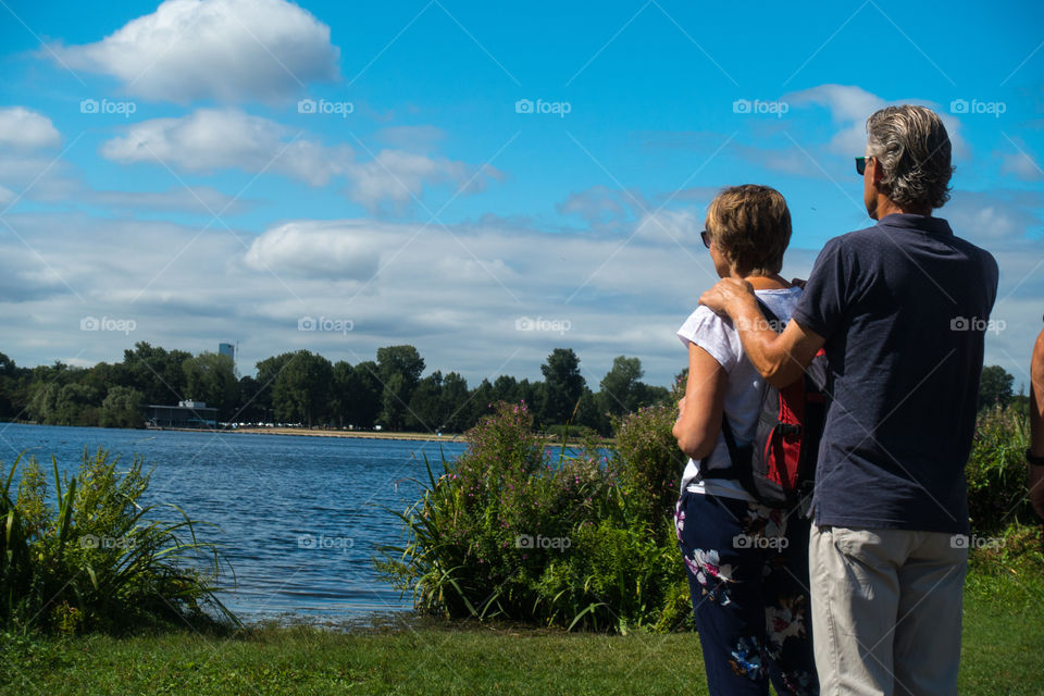 Man hands on woman shoulder standing against the sky by the lake 