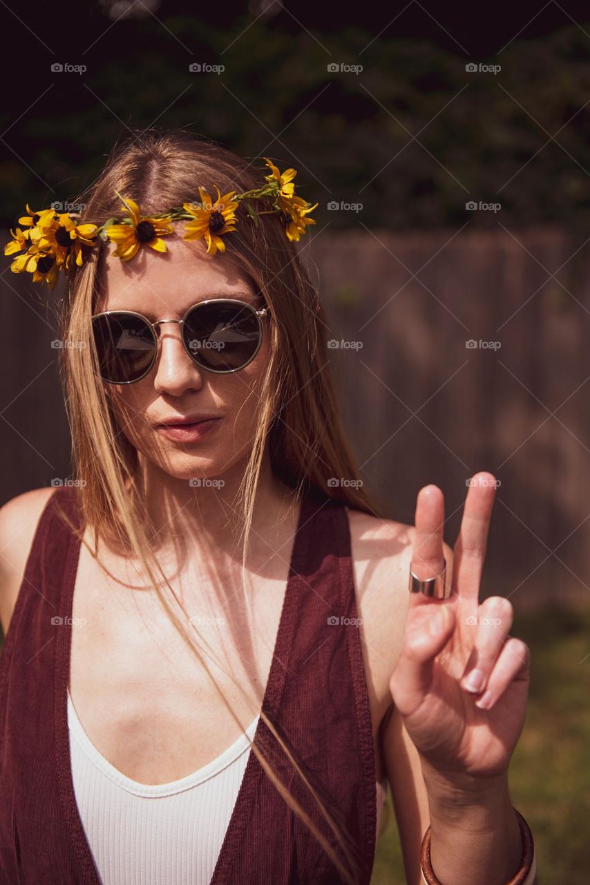 Young woman wearing retro sunglasses and a crown of flowers while giving a peace sign 