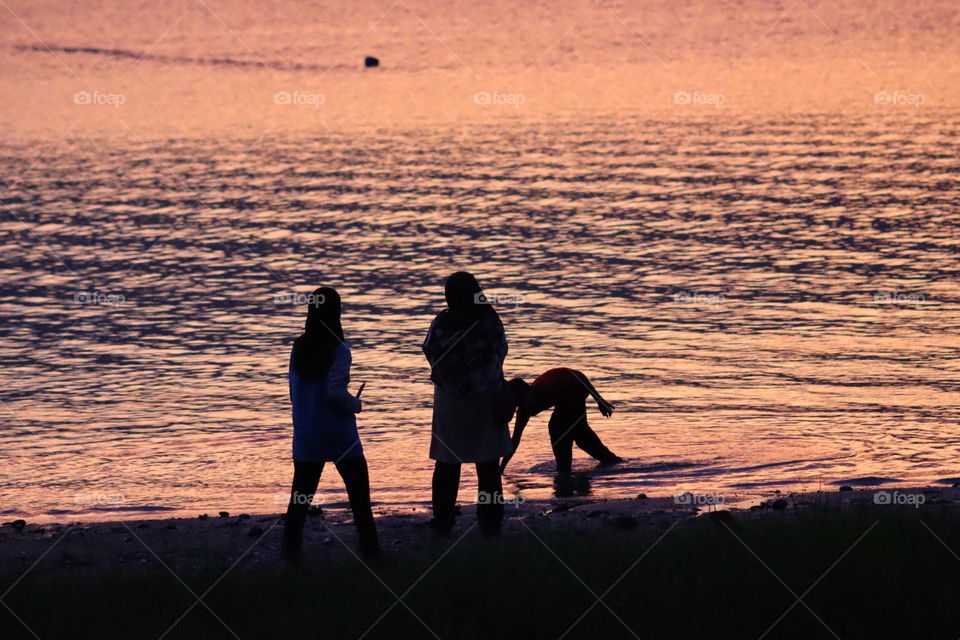 Silhouette of people playing in the water by the lake at sunset. Picnic by the lake 