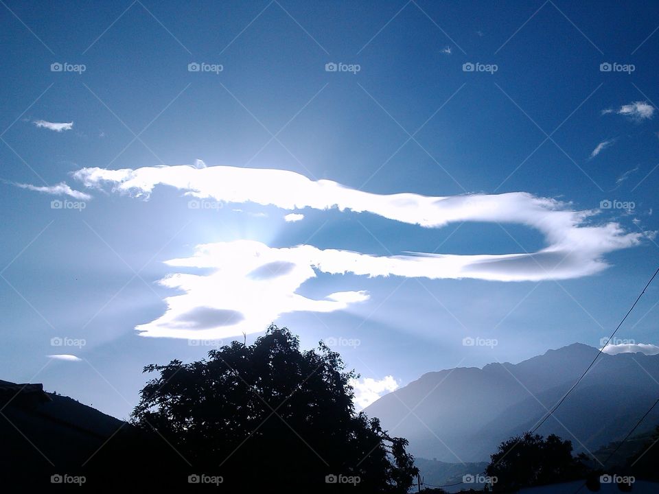 Despertar de una interrogante, se ve los destellos de luz sobre las nubes, el cielo despejado, las montañas a su alrededor y una sola nube que forma un signo de interrogación.