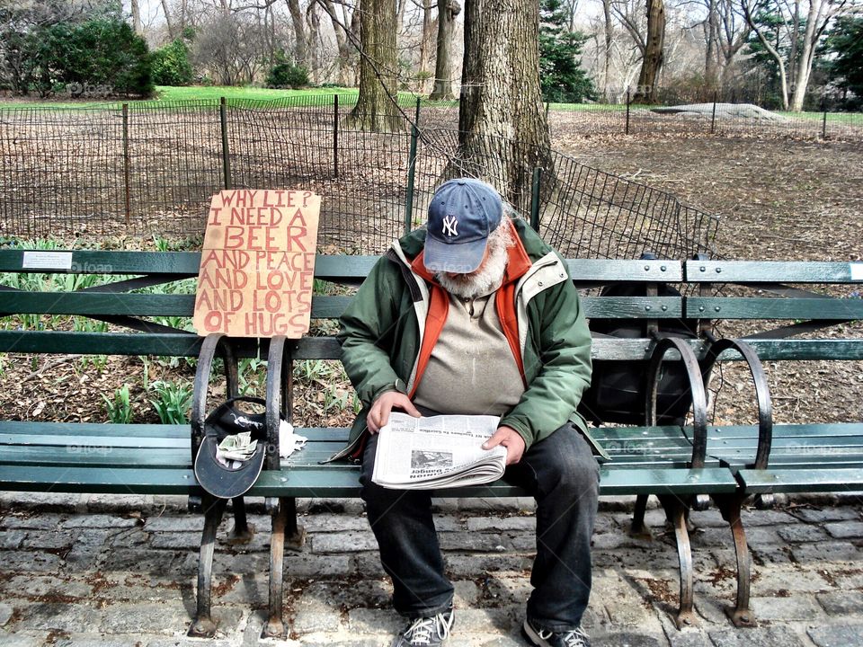 Beggar with an honest message sitting on a bench in Central Park