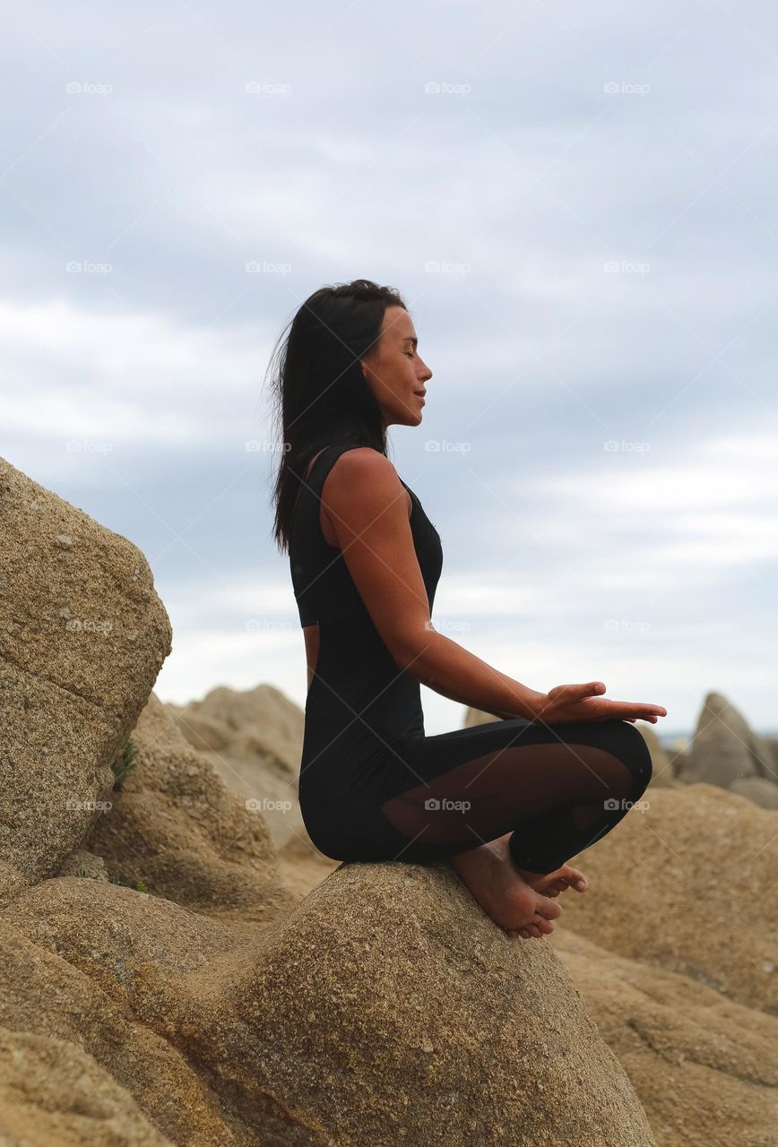 a girl in a black suit for sports, sits on the stones by the sea, meditates. complete calmness, relaxation, balance and harmony