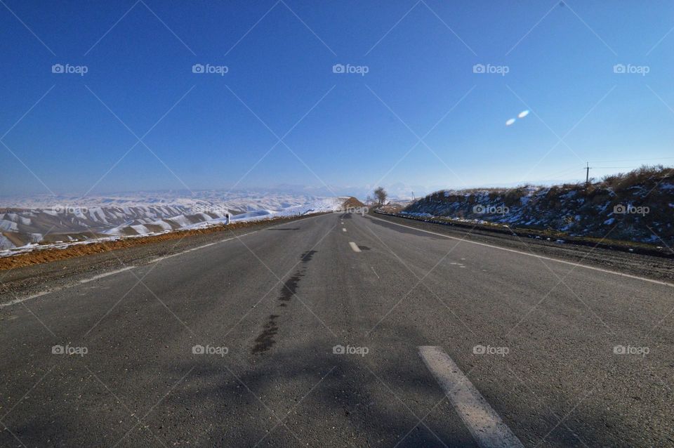 a wide roadbed with white markings goes at an altitude of 4,000 m on a par with the white snow-covered ridges of the Pamir mountains. view from the car.