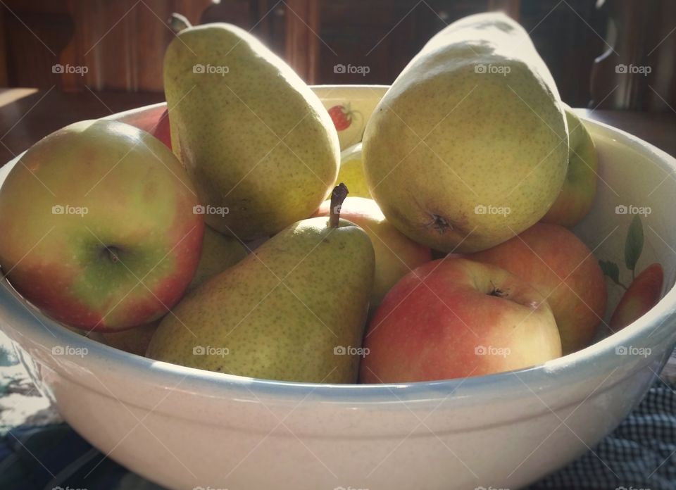 Pears and apples in a fruit bowl on a table in the morning light