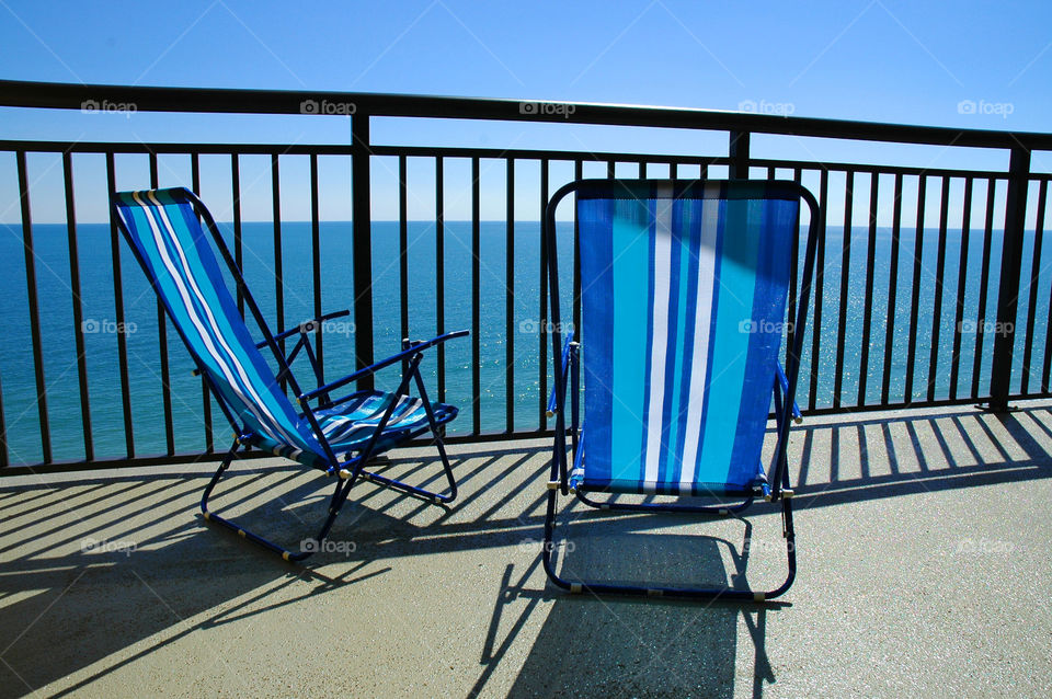 Two beach chairs. Two beach chairs sit on the balcony overlooking the ocean