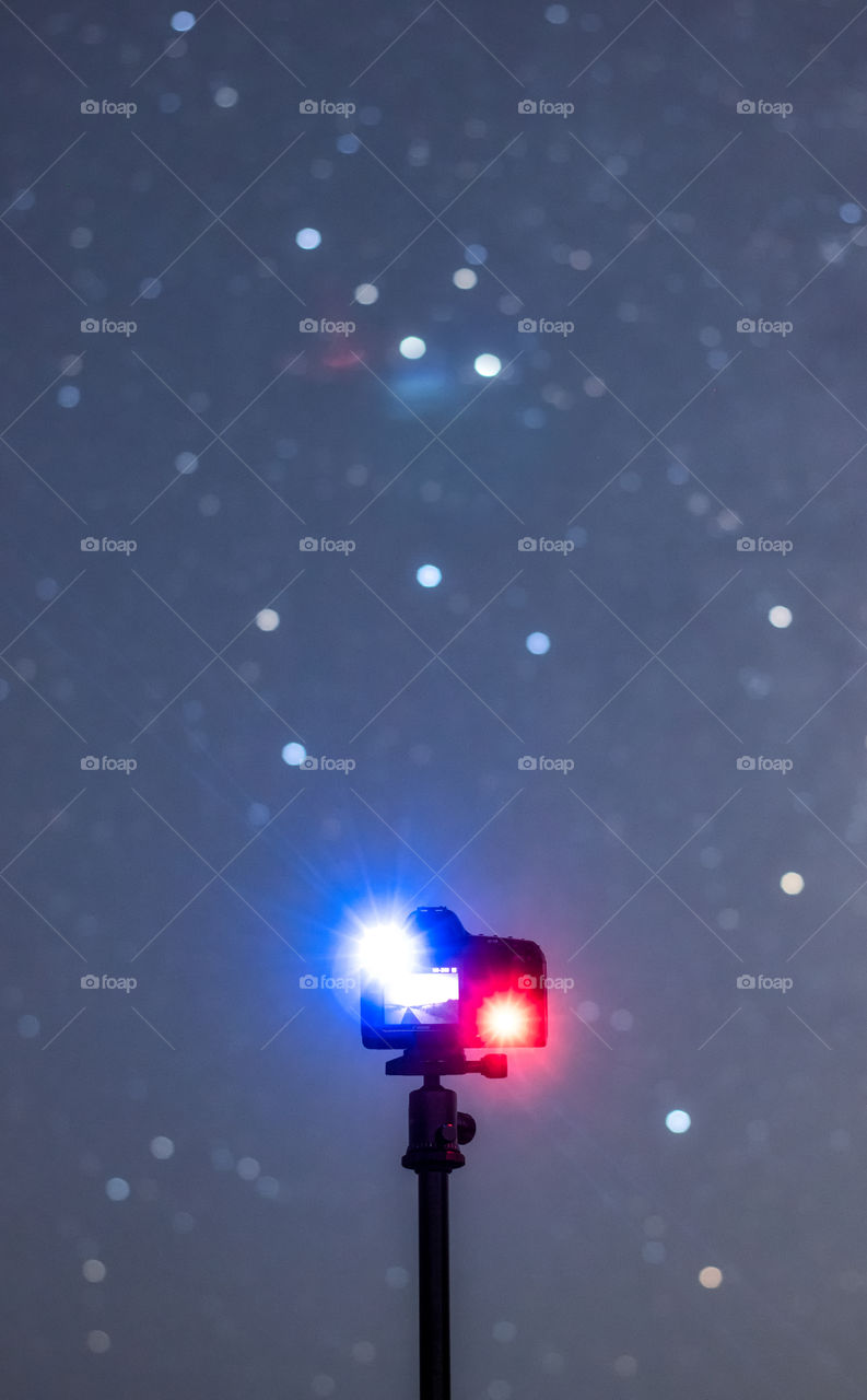 A camera taking photos of stars on a clear night sky. Shallow depth of field with the camera in focus and stars blurry.