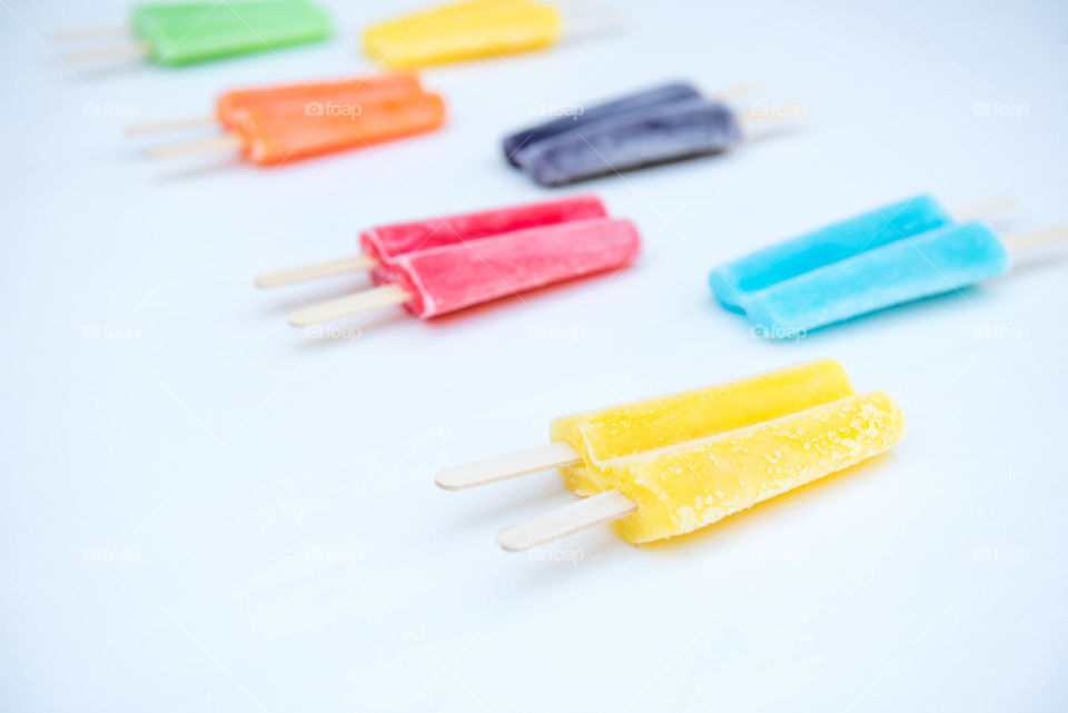 Rows of frosted, brightly colored frozen popsicles placed in a pattern on a white table